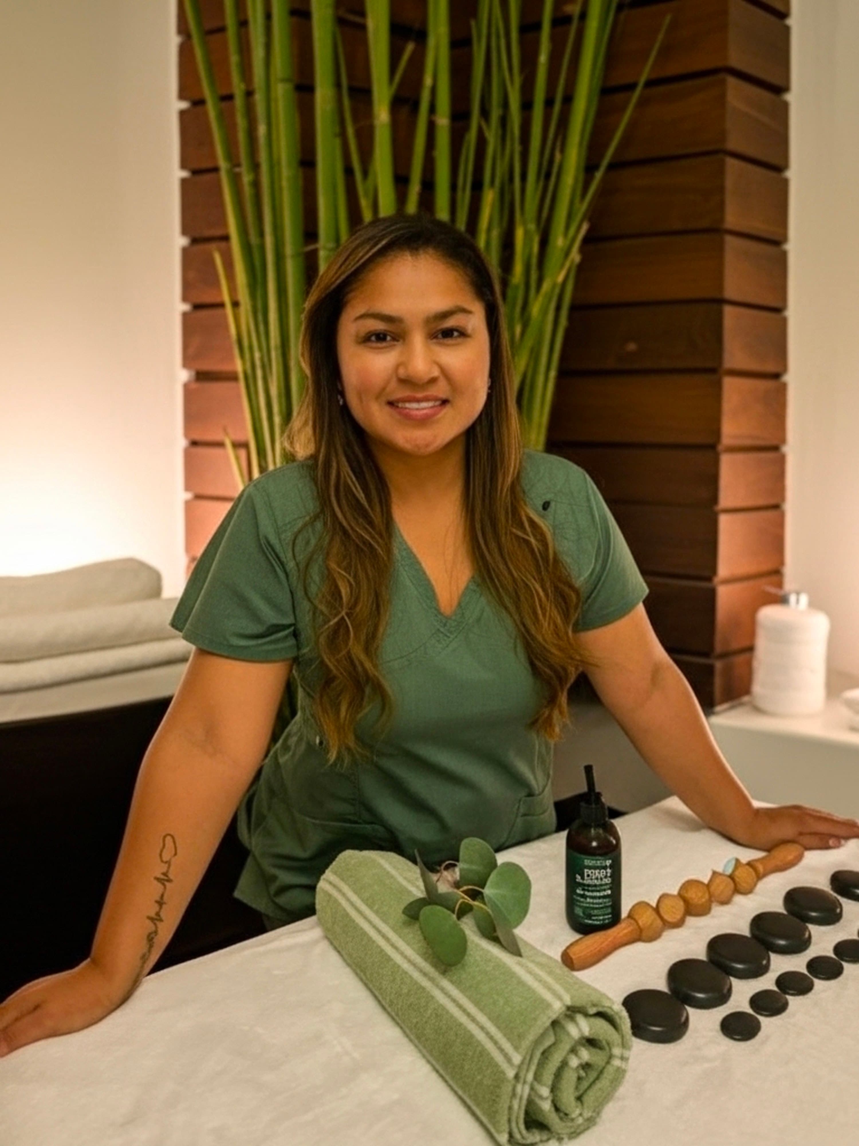 Sandy wearing green scrubs beside a prepared massage table.